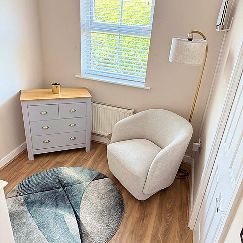 A bedroom reading corner at Hammond House with a chair, shelf and lamp beside the window.